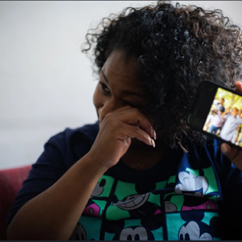 woman holds up cell phone showing photo of her children while wiping away tears